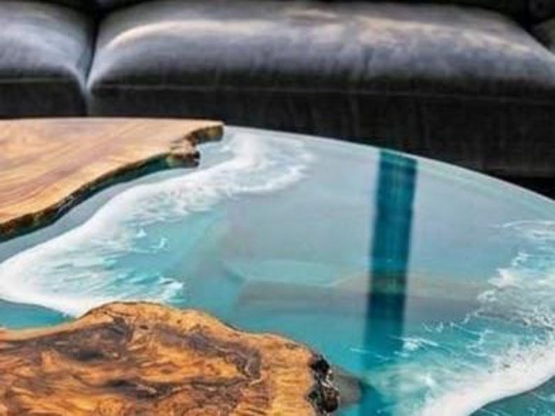May include: A unique coffee table with a live edge wood design and a clear epoxy resin top, creating a coastal ocean wave effect. The wood has a natural, warm brown color, contrasting with the blue and white resin. The table is a decorative furniture piece.