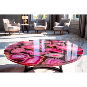 May include: A circular coffee table with a polished, reflective surface. The tabletop showcases a striking pink agate pattern with gold detailing. The table is supported by a black metal base and is in a bright room with seating.