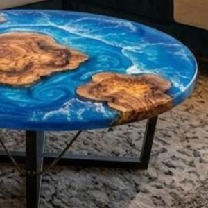 May include: Round coffee table with a blue epoxy resin top, featuring natural wood inlays. The table has a dark metal base. The wood inlays have a natural, organic shape. The table's diameter is approximately 36 inches.