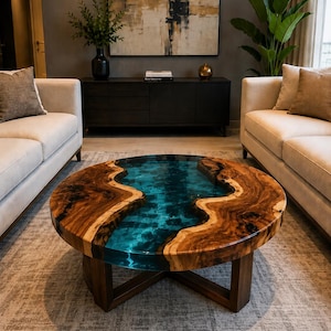 May include: Round coffee table with a wooden frame and a unique top. The table's surface features a river of blue resin flowing between two sections of natural wood. The wood has a rich, brown color, and the table is supported by a dark wooden base.
