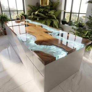 Pode incluir: Ilha de cozinha moderna com um design único. A bancada apresenta uma placa de madeira embutida em resina azul clara, criando um efeito de rio. A base é branca com gavetas integradas, e a sala é preenchida com luz natural.