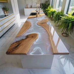 May include: A modern kitchen island with a unique design. The countertop features a light-colored epoxy resin river flowing between sections of natural wood. The island is supported by a white base and has a glossy finish.