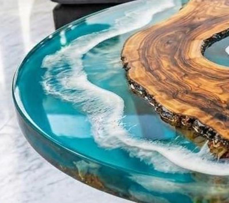 May include: A unique, handcrafted coffee table with a wood slab and epoxy resin design. The table features a natural wood grain section and a turquoise resin river, creating a wave-like effect. The table's dimensions are not visible in the image.