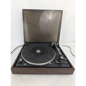 May include: A vintage Dual CS 505-1 turntable with a dark wood grain finish. The turntable features a black platter, a tonearm, and a clear dust cover. The Dual logo is visible on the cover.