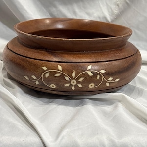 Puede incluir: Un cuenco redondo de madera con acabado marrón oscuro. El cuenco presenta un diseño floral y de vid incrustado en un color más claro alrededor del exterior. El cuenco tiene una forma ancha y poco profunda con un borde ligeramente elevado.