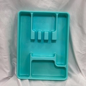 May include: A turquoise plastic cutlery tray with multiple compartments for organizing silverware. The tray has a rectangular shape with rounded corners and a smooth surface. It is designed to fit inside a kitchen drawer.