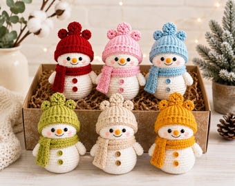 May include: Six crocheted snowman figurines arranged in a cardboard box. Each snowman has a white body, a small orange nose, black eyes, and pink cheeks. They wear matching colored hats with three small pom-poms and scarves in red, pink, blue, green, beige, and yellow.