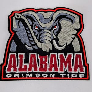 Könnte beinhalten: Gestickter Aufnäher mit dem Logo der Alabama Crimson Tide. Der Aufnäher hat einen schwarzen Hintergrund mit rotem Rand. Das Logo zeigt einen grauen Elefanten mit roten Augen über dem Wort "ALABAMA" in Rot und "CRIMSON TIDE" in Weiß.