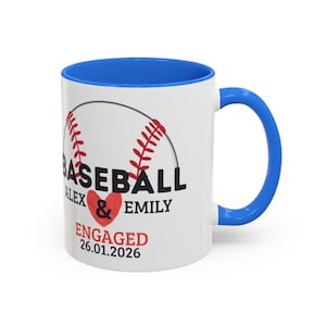 Peut inclure: Mug en céramique blanche avec intérieur et anse bleus. Le mug présente un motif de baseball avec le mot "BASEBALL" et les noms "ALEX & EMILY" avec un symbole de cœur. Le texte "ENGAGÉ 26.01.2026" est également affiché.