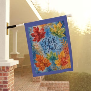 May include: A rectangular garden flag with a blue border featuring a watercolor design of autumn maple leaves in shades of red, orange, yellow, and green against a blue background. The text Hello Fall is printed in dark blue script in the center.