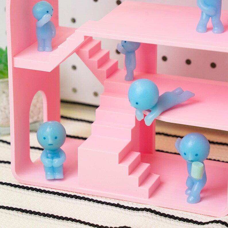 May include: A pink dollhouse with multiple levels and stairs, populated by small blue figurines in various poses. The dollhouse has a minimalist design, with a few figurines on each level. The overall aesthetic is playful and whimsical.