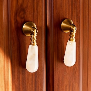 Puede incluir: Primer plano de un armario de madera con dos tiradores de latón y piedra blanca. Las puertas del armario son de madera marrón oscuro con vetas verticales. Los tiradores tienen un diseño decorativo.