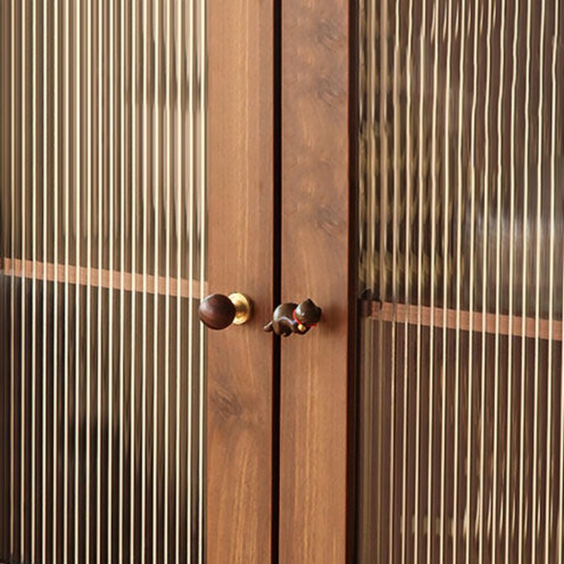 Puede incluir: Primer plano de un armario de madera con dos puertas. Las puertas son de color marr&oacute;n oscuro y tienen paneles de vidrio decorativos con l&iacute;neas verticales. El armario presenta dos tipos diferentes de pomos: un pomo redondo de madera y un pomo peque&ntilde;o con forma de animal.