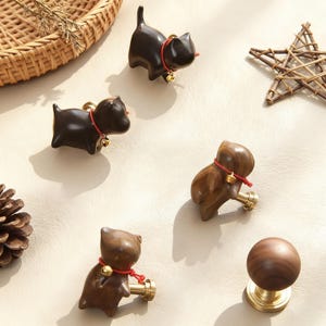 Puede incluir: Una colecci&oacute;n de tiradores y pomos decorativos de madera para armarios. Los pomos tienen forma de gatos y perros, con collares rojos y peque&ntilde;as campanas doradas. Los tiradores tienen un acabado de lat&oacute;n. La paleta de colores incluye marr&oacute;n oscuro y marr&oacute;n claro.