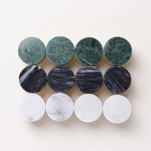 Może przedstawiać: Dwanaście okrągłych gałek do szafek z marmuru w odcieniach zieleni, czerni i bieli. Gałki ułożone są w trzech rzędach po cztery, prezentując naturalne żyłkowanie i wzory kamienia. Te dekoracyjne gałki są idealne do dodania elegancji meblom.