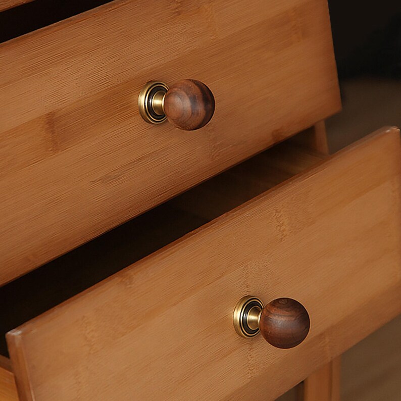 Puede incluir: Primer plano de dos cajones de madera con pomos redondos de color marr&oacute;n oscuro y herrajes dorados. Los cajones son de bamb&uacute; marr&oacute;n claro, con vetas visibles. Un caj&oacute;n est&aacute; parcialmente abierto.