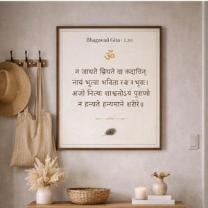May include: A framed print of the Bhagavad Gita 2.20 text in Sanskrit, with a gold Om symbol. A straw hat and tote bag hang on the wall. A small vase with dried flowers, a woven basket, and a candle sit on a wooden shelf.