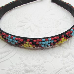 May include: A beaded headband with a black base. The headband is adorned with rows of small, colorful beads in red, yellow, blue, and black. The beads are tightly arranged, creating a textured and vibrant pattern. This accessory is suitable for various occasions.