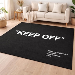 Può includere: Un tappeto rettangolare nero con le parole "KEEP OFF" in grandi lettere maiuscole bianche. Il tappeto ha anche il testo "IKEA c/o Virgil Abloh Flooring Almhult, Svezia c.2019". Il tappeto è posto su un pavimento in legno.