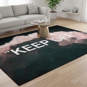 Può includere: Un tappeto rettangolare con un design a nuvole verde scuro e rosa. Le parole "KEEP OFF" sono in grandi lettere bianche. Il tappeto è su un pavimento in legno chiaro.
