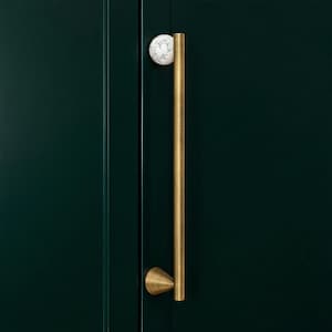 May include: A gold-toned cabinet pull with a white and grey marble sphere at the top. The long, vertical handle is mounted on a dark green cabinet door. The pull has a conical base.