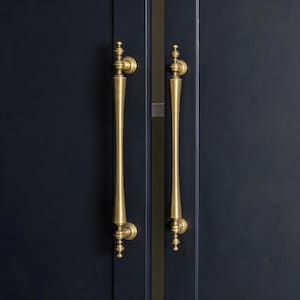 May include: Two antique brass door handles with a decorative design. The handles are long and slender, with a slightly curved shape and ornate detailing at the top and bottom. They are mounted on a dark blue door.