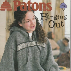 May include: A gray hooded sweater with a white and black stripe across the chest. The sweater is being worn by a person with long brown hair. The text "Patons Hanging Out" is visible at the top of the image. The text "Easy knits for girls and guys ages 8 to 15 years." is visible at the bottom of the image. The text "Featuring Patons Canadiana, Patons Canadiana Tweeds and Patons Shetland Ragg K.W." is also visible at the bottom of the image.