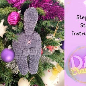 May include: A handmade, gray plush bunny Christmas ornament with a pink cross on its back, hanging on a decorated Christmas tree. The tree is adorned with ornaments and tinsel. Text on the right says "Step by Step instruction".