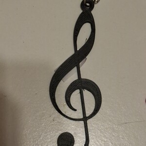 May include: A black treble clef keychain. The musical symbol is made of a solid material and attached to a silver chain. The keychain is a simple, yet elegant accessory for music lovers.