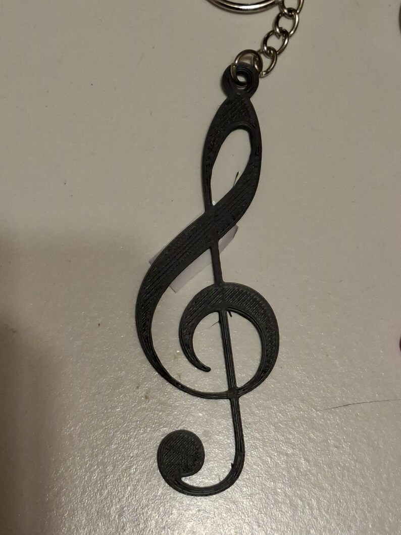 May include: A black treble clef keychain. The musical symbol is made of a solid material and attached to a silver chain. The keychain is a simple, yet elegant accessory for music lovers.