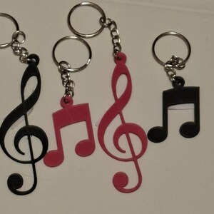 May include: Keychains featuring musical notes and treble clef symbols in black and red. Each keychain has a silver-colored ring and chain. The keychains are made of a flat, solid material.