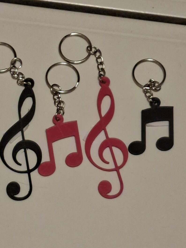 May include: Keychains featuring musical notes and treble clef symbols in black and red. Each keychain has a silver-colored ring and chain. The keychains are made of a flat, solid material.