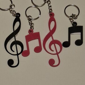 May include: Keychains featuring musical notes in black and pink. The keychains have a silver chain and ring. The musical notes include a treble clef and eighth notes. The keychains are made of a solid material.