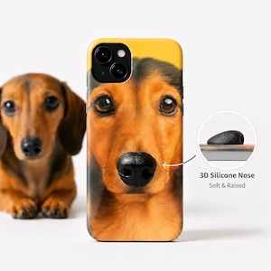 May include: A phone case featuring a high-resolution close-up of a brown and black dachshund face. The case includes a black 3D silicone nose that is soft and raised. The design highlights the dog's large dark eyes and detailed fur texture.