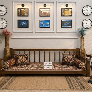 May include: A wooden daybed with a spindle backrest, featuring a patterned seat cushion and two matching square throw pillows with two cylindrical bolster pillows. A small white sign on the seat displays the text THE ANATOLIAN SOUL.