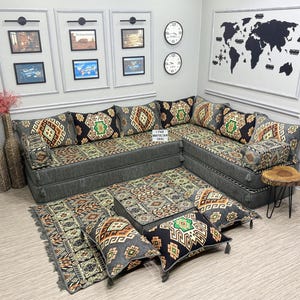 Puede incluir: Un sofá seccional gris con cojines estampados y cojines de suelo a juego. Los cojines presentan diseños geométricos en tonos marrón, verde y negro. Relojes decorativos y obras de arte enmarcadas adornan las paredes, con un mapa del mundo.