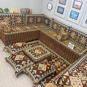 May include: A large L-shaped floor sofa set featuring brown fabric with a geometric diamond pattern in blue, white, and gold. The set includes back cushions, floor cushions, and a small square sign that reads THE ANATOLIAN SOUL in black text.