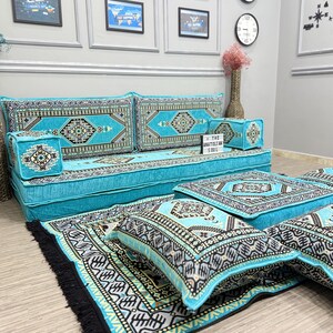 May include: A floor seating set featuring a long turquoise sofa, matching floor cushions, and a rug, all decorated with intricate black, white, and gold geometric patterns. A small sign on the sofa displays the text The Anatolian Soul.