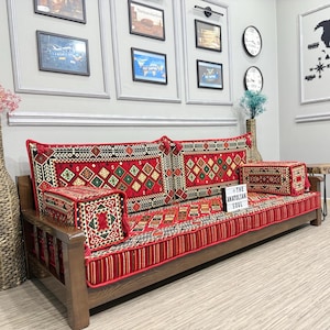 May include: A wooden sofa with red and patterned cushions and a matching ottoman. The cushions feature a geometric design with red, green, and black accents. The sofa is in a room with framed pictures and a world map.