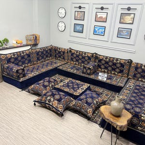 Puede incluir: Un gran juego de sofás modular con base azul oscuro y cojines estampados. Los cojines presentan un diseño floral repetido en tonos dorados, marrones y crema. El conjunto incluye múltiples secciones de asientos y cojines decorativos.