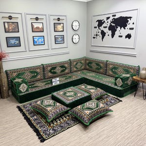 May include: A green corner sofa with patterned cushions and pillows, set on a patterned rug. The room includes framed pictures, clocks, and decorative vases, creating a comfortable living area.