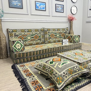 May include: A floor seating set featuring a long sofa cushion, a square floor cushion, and several throw pillows, all upholstered in a grey fabric with a geometric pattern in orange, green, and white. A small sign reads THE ANATOLIAN SOUL.