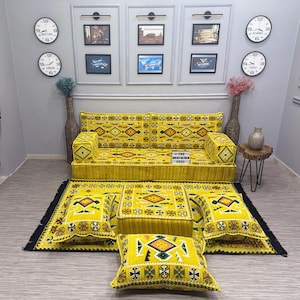 Puede incluir: Un juego de sofá amarillo estampado con alfombra y cojines a juego. El juego presenta diseños geométricos en negro, naranja y verde. El sofá tiene dos reposabrazos cuadrados a juego. La alfombra y los cojines tienen un borde negro.