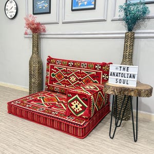 May include: A red floor cushion and backrest set with geometric patterns in green, orange, and white. A matching cube-shaped ottoman and a small side table with the text "THE ANATOLIAN SOUL" complete the scene.