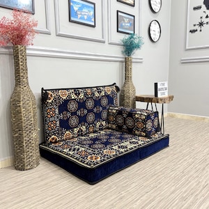 Könnte beinhalten: Ein niedriges, marineblaues Bodensitz-Set mit einem Muster in Blau-, Gold- und Orangetönen. Das Set umfasst eine Rückenlehne, ein Sitzkissen und ein passendes Kissen. Zwei dekorative Vasen mit Trockenblumen sind ebenfalls zu sehen.