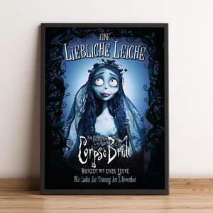 以下が含まれることがあります： アニメ映画「ティム・バートンのコープスブライド」のフレーム入りポスター。青い肌の長い黒髪とベールをまとった花嫁が、青い背景に描かれています。タイトルとその他のテキストが表示されています。