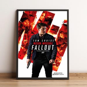 Może przedstawiać: Oprawiony plakat filmowy do filmu "Mission: Impossible - Fallout" z Tomem Cruise'em. Plakat ma czerwono-białe tło ze zdjęciami innych aktorów. Tytuł filmu jest dużymi, pogrubionymi literami, z miesiącem premiery lipiec.