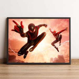 K&ouml;nnte beinhalten: Gerahmtes Kunstwerk mit zwei Spider-Man-Charakteren in dynamischen Posen vor einem Sonnenuntergangshintergrund. Ein Spider-Man tr&auml;gt einen schwarz-roten Anzug, der andere einen klassischen rot-wei&szlig;en Anzug, beide benutzen Spinnweben. Das Kunstwerk wird auf einer Holzoberfl&auml;che ausgestellt.