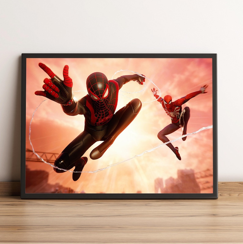 K&ouml;nnte beinhalten: Gerahmtes Kunstwerk mit zwei Spider-Man-Charakteren in dynamischen Posen vor einem Sonnenuntergangshintergrund. Ein Spider-Man tr&auml;gt einen schwarz-roten Anzug, der andere einen klassischen rot-wei&szlig;en Anzug, beide benutzen Spinnweben. Das Kunstwerk wird auf einer Holzoberfl&auml;che ausgestellt.