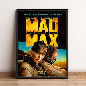 May include: A framed movie poster for Mad Max: Fury Road. The poster features the film's title in large, yellow, distressed lettering. The image shows two people in the foreground, with the text "THE FUTURE BELONGS TO THE MAD" at the top.